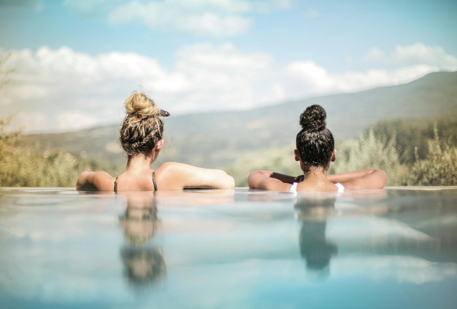 Two women relaxing in a pool with scenic mountain and countryside views.