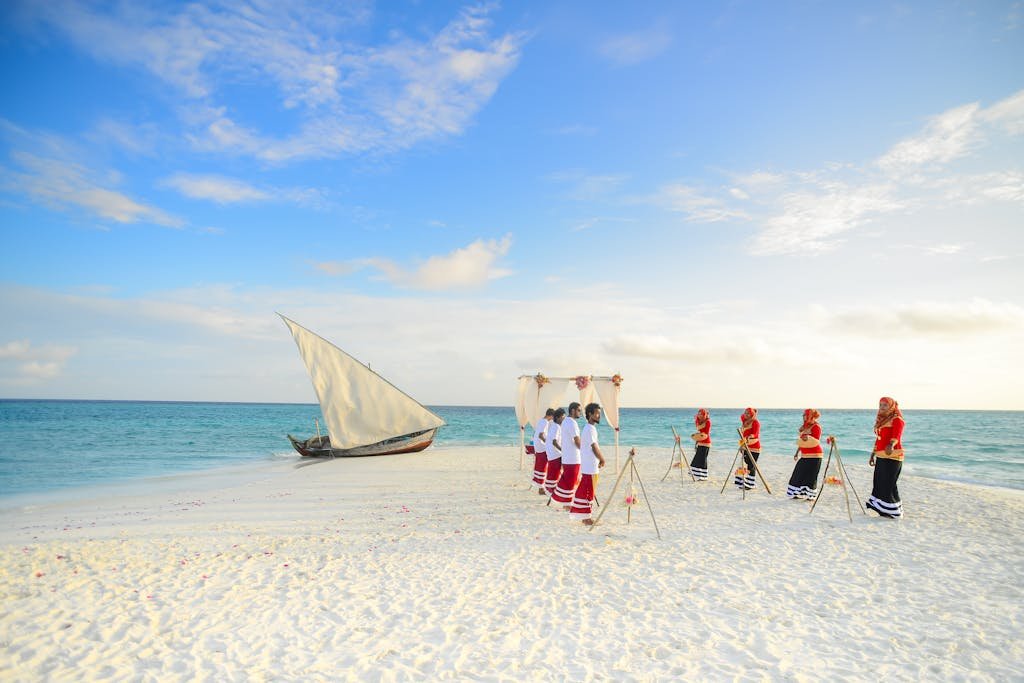 Vibrant Maldivian wedding on a white sandy beach with traditional attire and a sailboat.