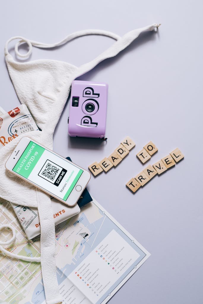 Flat lay of travel essentials including smartphone, health passport, map, and scrabble tiles with 'Ready to Travel'.