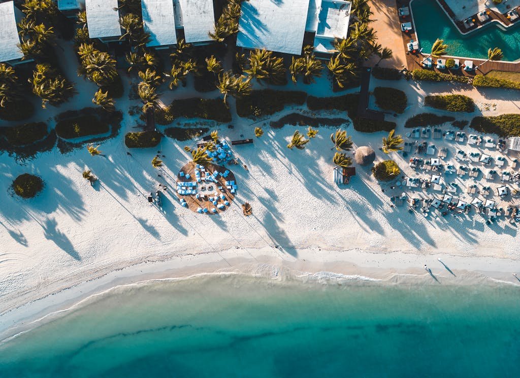 Stunning aerial view of a tropical beach resort in Playa del Carmen, Mexico with palm trees and clear blue waters.